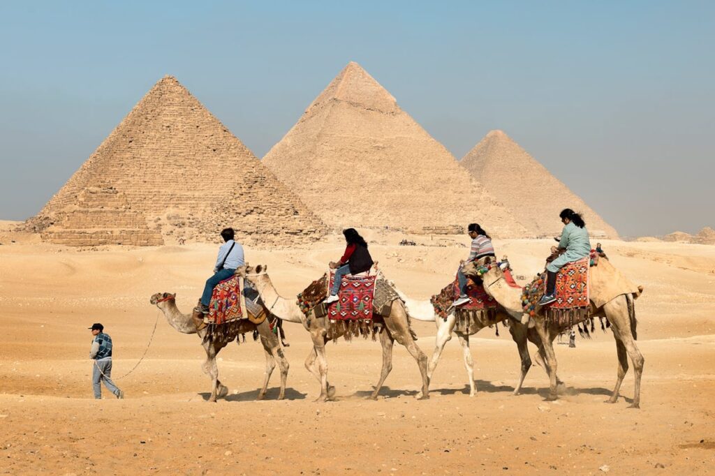 Four People Riding on Camels Across the Pyramids